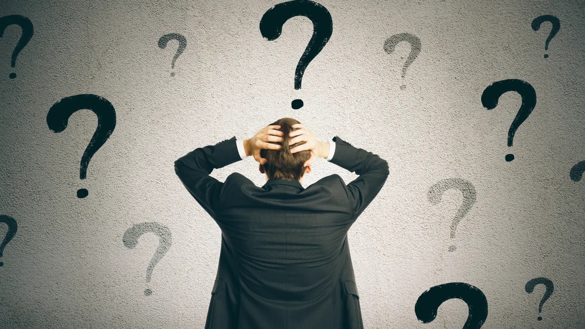 Businessman holding his head while standing among question marks, symbolizing choice of Geneo alternatives